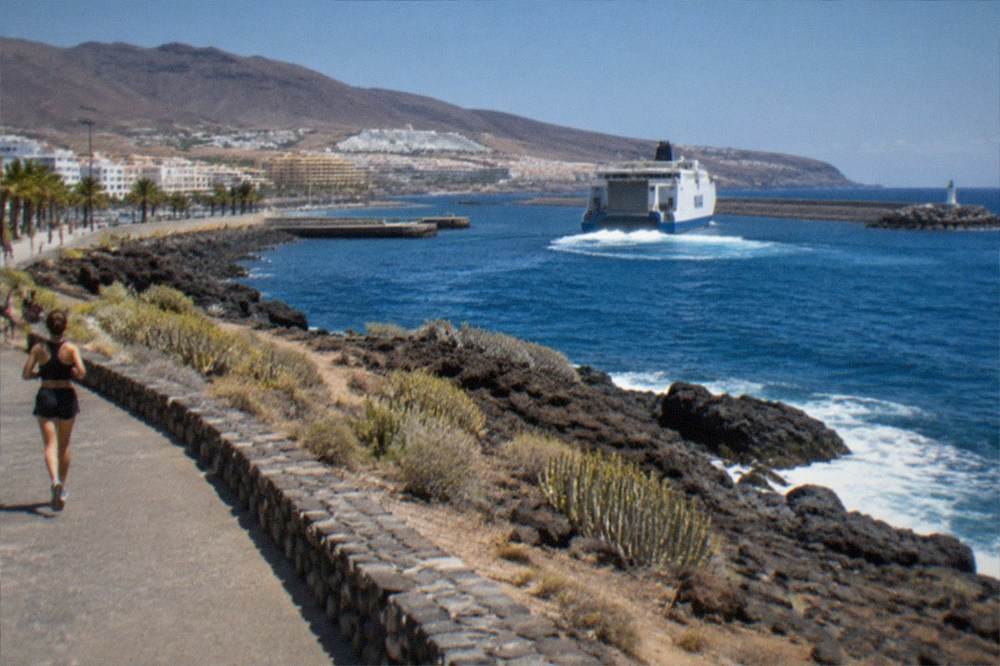 A large ferry leaving a harbour with a town visible on the hillside