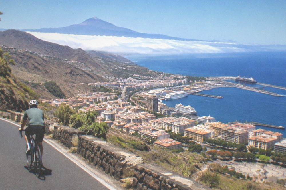 A cyclist on a mountain road above the clouds with Teide in the distance