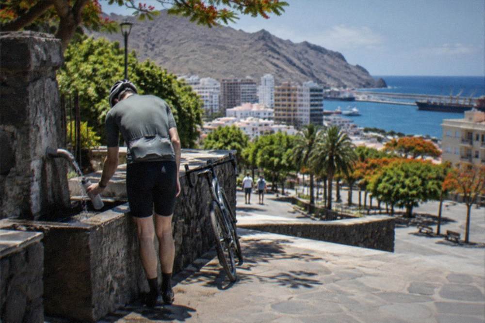 A cyclist filling a water bottle at a mountain village fountain