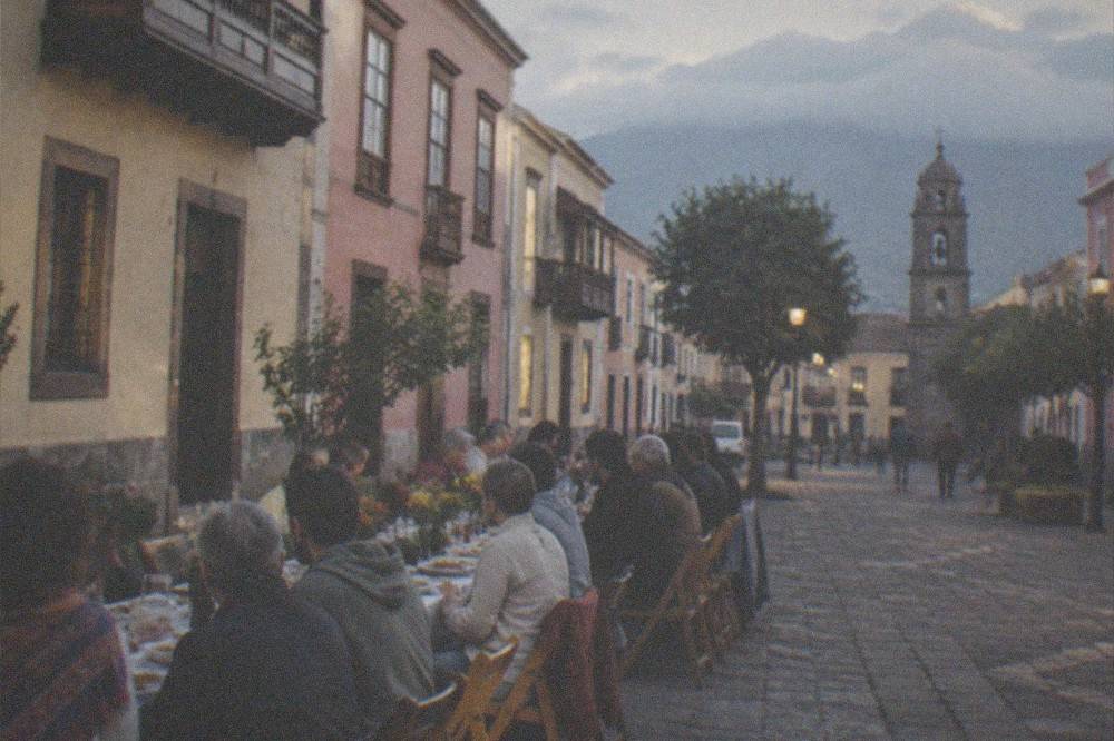 A long table of people sharing a Canary Island meal outdoors in the evening