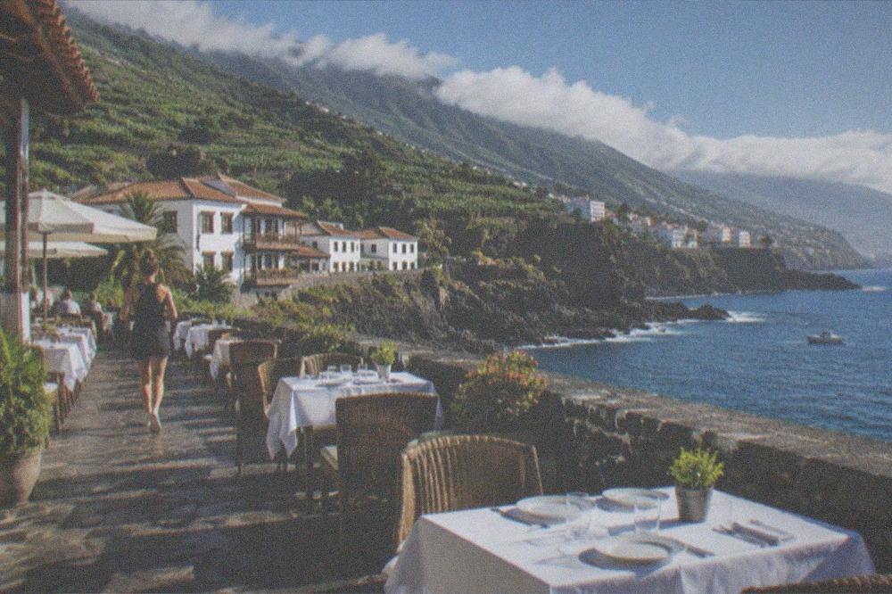 An outdoor restaurant terrace by the sea at Puerto de la Cruz with tables set for lunch under a blue sky