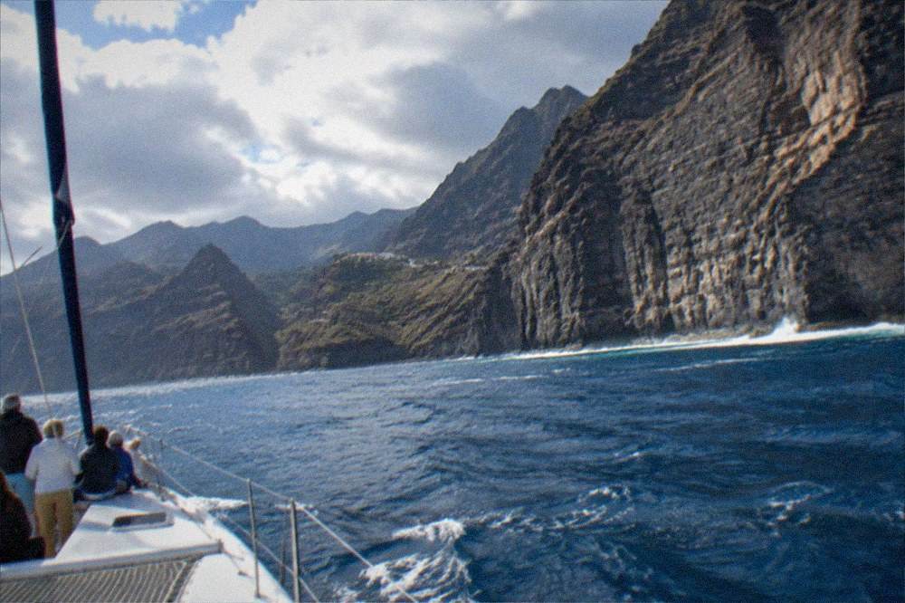 A catamaran sailing close to the tall sea cliffs of Los Gigantes, passengers watching the water