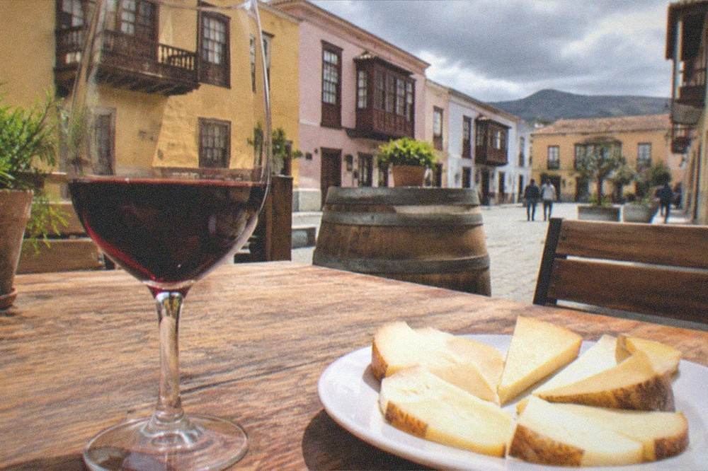 A glass of red wine and a plate of local cheese on a wooden table at a Tenerife winery