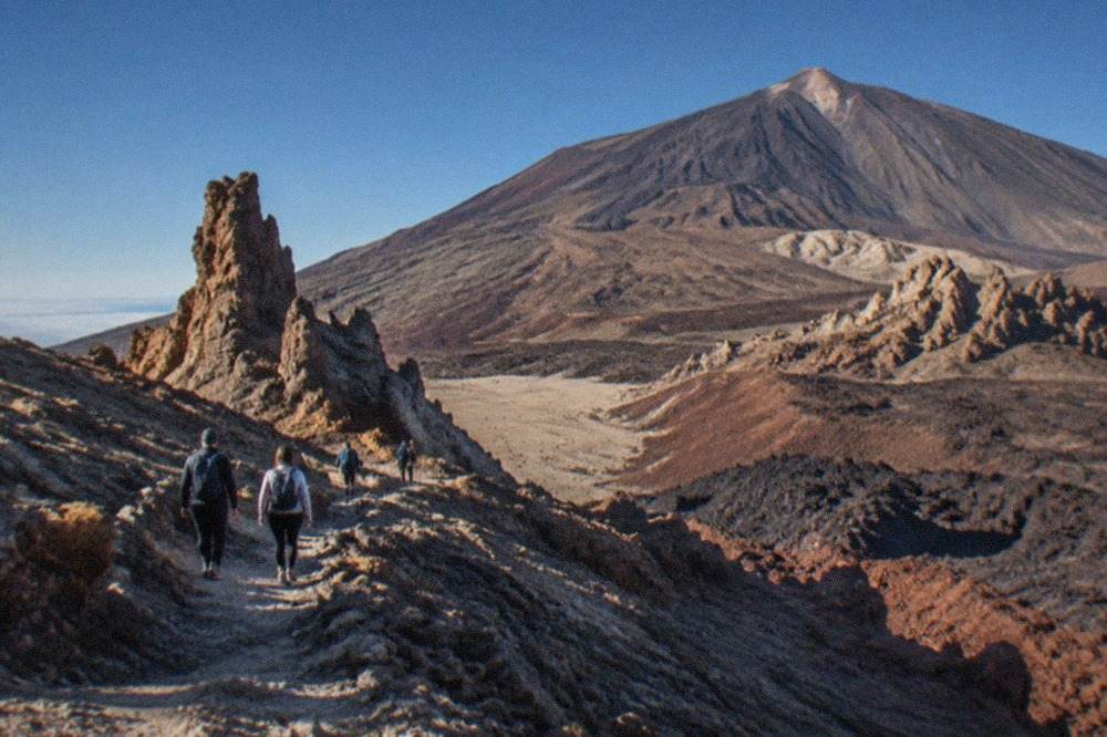 Hikers walking a rocky volcanic trail on Mount Teide under a clear blue sky