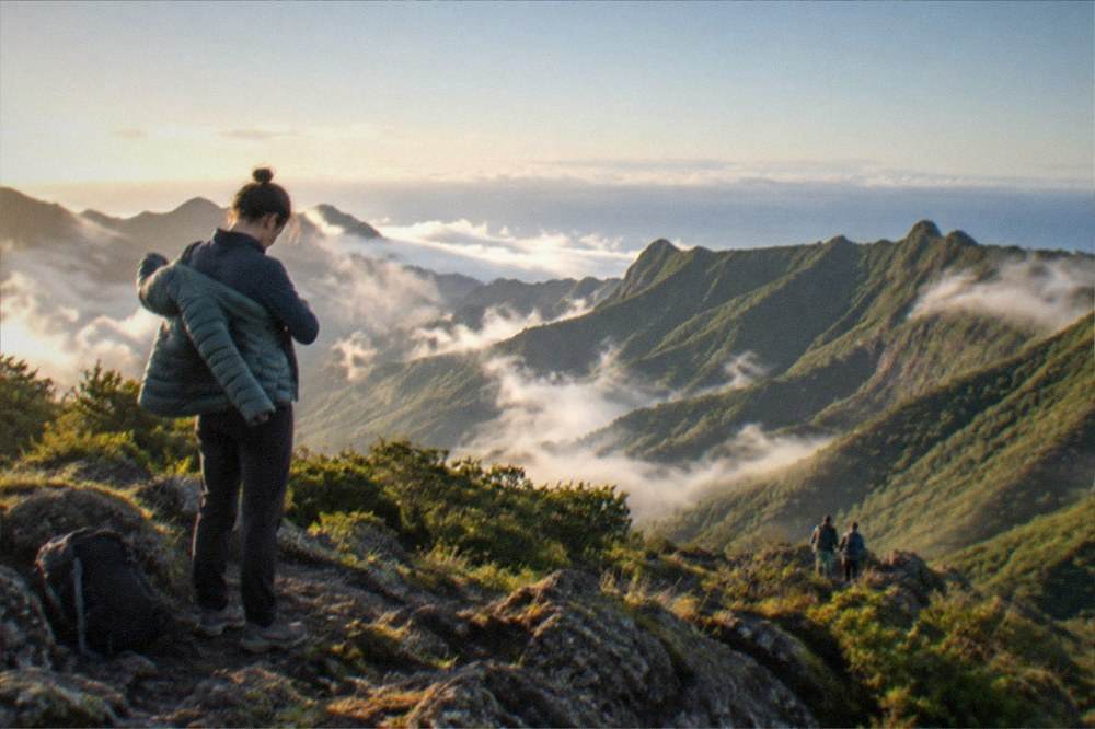A hiker putting on a warm layer at a rocky viewpoint above the clouds
