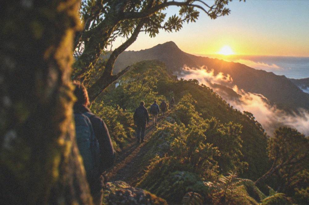 A group of hikers following a guide along a ridge path at sunrise