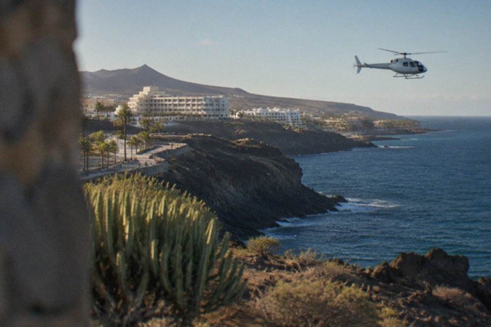 A light helicopter in flight above a volcanic landscape with reddish rock formations