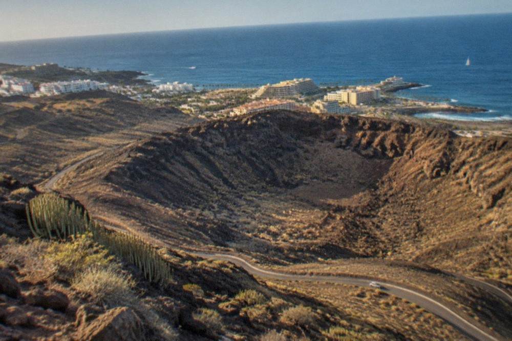An aerial view of a volcanic crater with rocky slopes and a winding road below