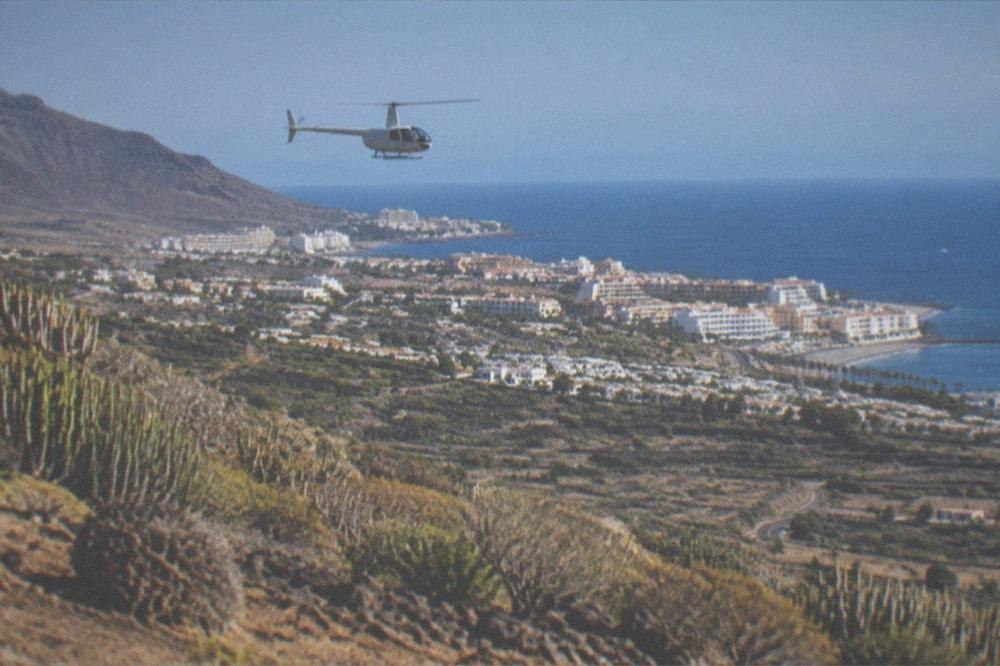 A helicopter flying above a green valley with terraced fields and a town in the distance