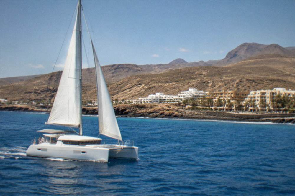 A catamaran sailing near the coast with hotels along the shoreline