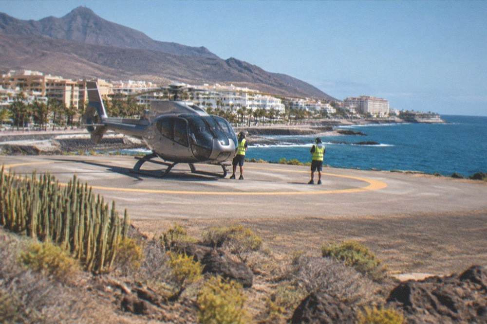 A helicopter on a paved helipad with ground crew standing nearby