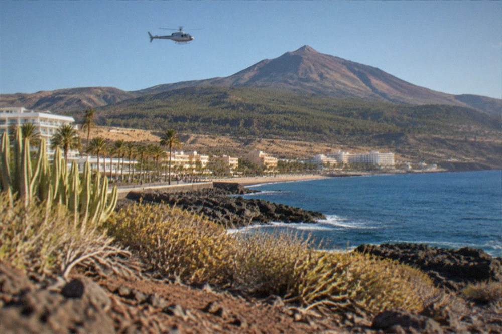 A helicopter flying above pine forest on the slopes of a volcano