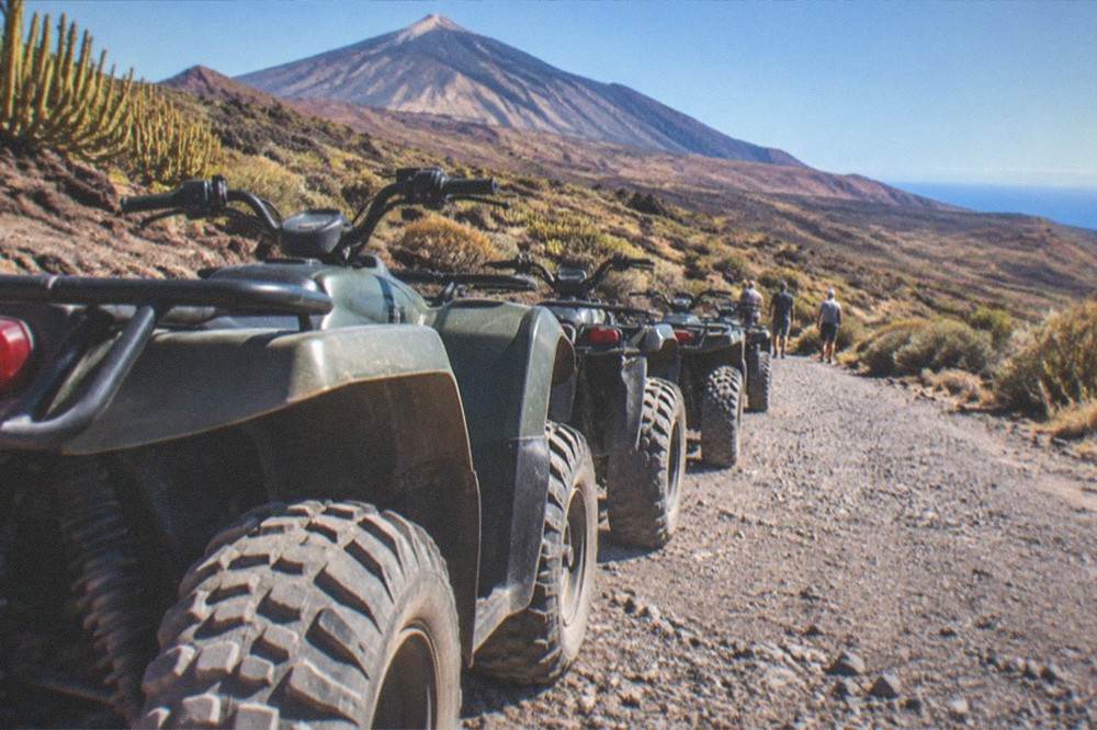 A line of quad bikes parked on a volcanic gravel track with Teide's cone rising in the background