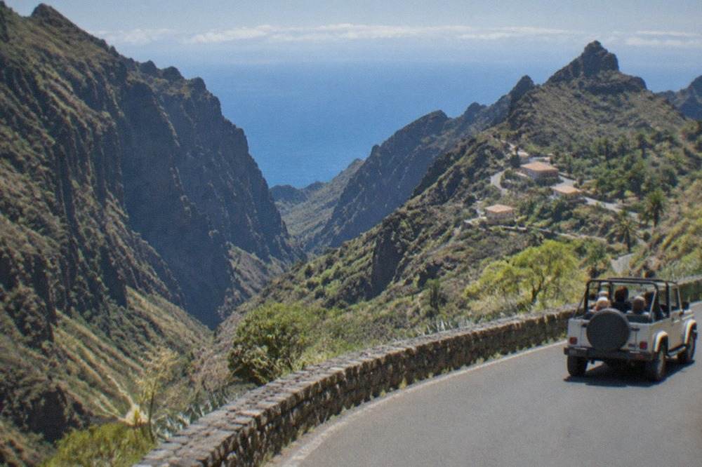 Open-top jeep on a winding mountain road above the clouds in Tenerife
