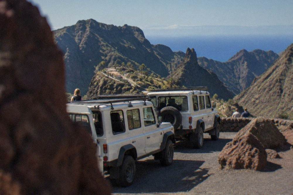 Convoy of safari jeeps parked at a volcanic viewpoint with red rock formations