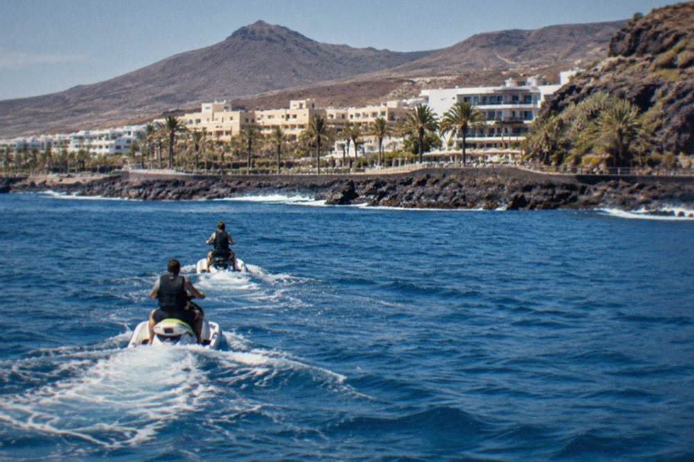 Two jet skis riding in single file across calm water with a guide in front near the Tenerife shoreline