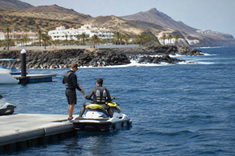 A rider in a buoyancy vest sitting on a jet ski during a briefing beside a marina pontoon