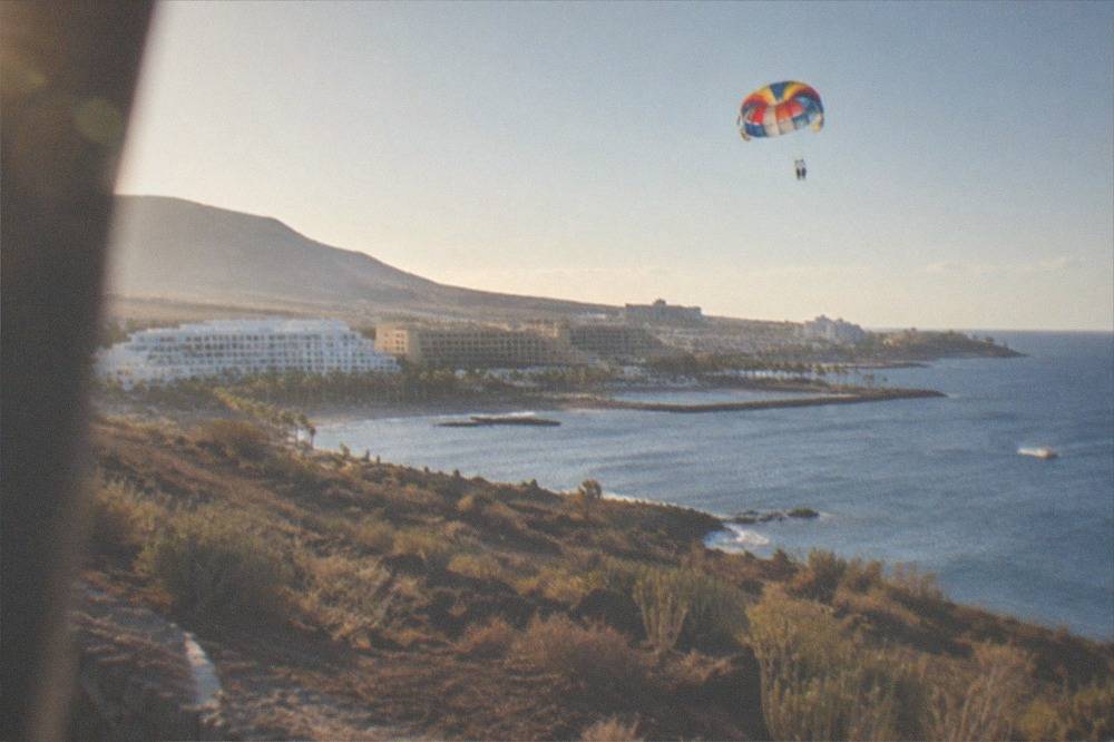 A parasailing parachute high above the Costa Adeje coastline with hotels and blue water below