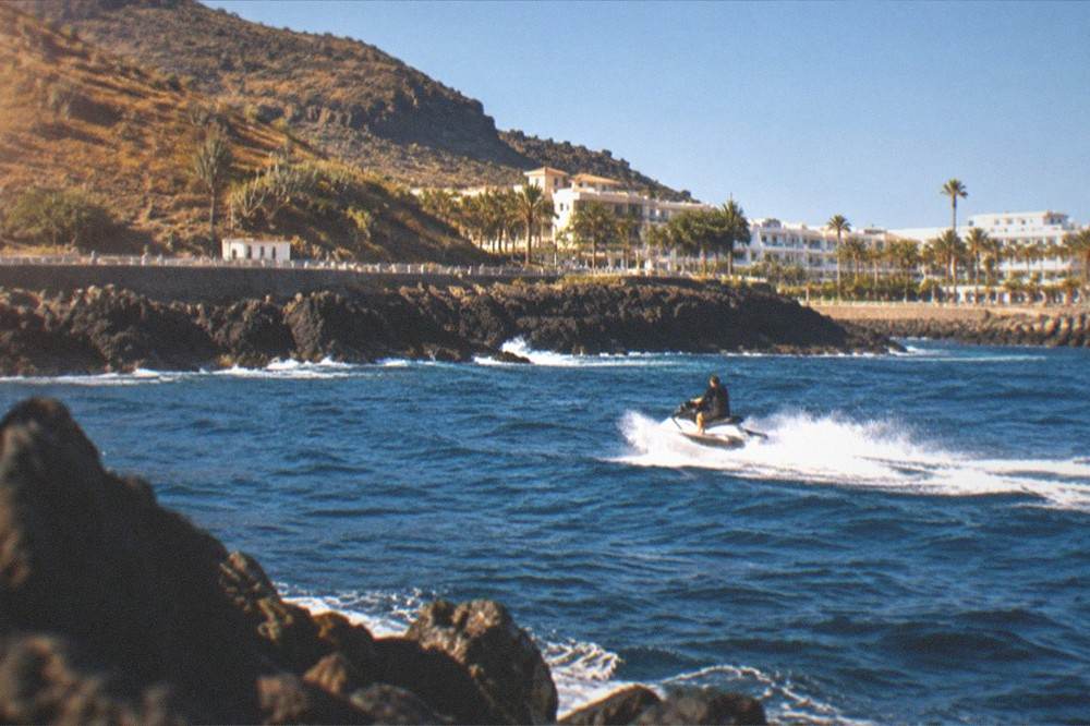 A jet ski at speed under a clear blue sky along a rocky Tenerife headland