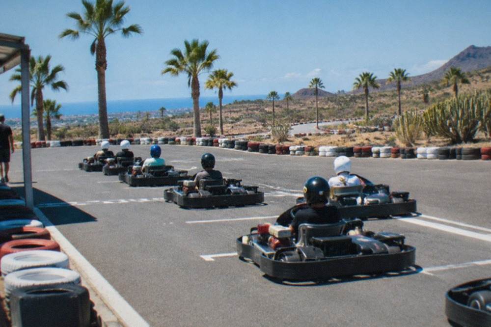 Karts lined up on a start line under a bright blue sky beside a palm-lined circuit