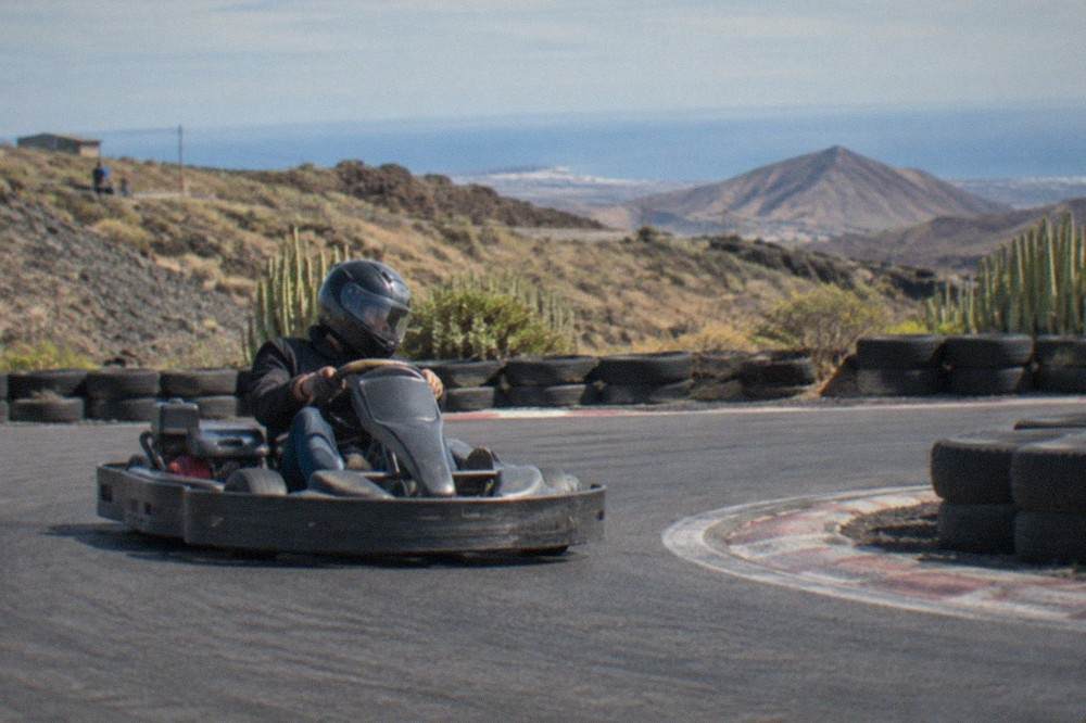 A driver in a full-face helmet steering a kart through a corner on an outdoor track