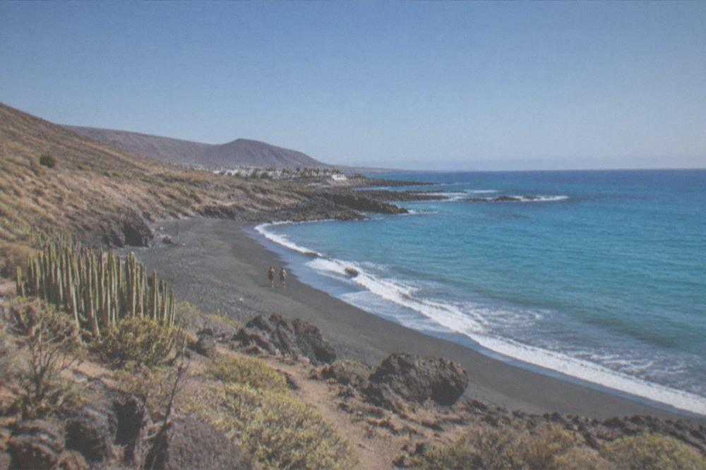 A calm turquoise sea breaking gently on a dark volcanic beach under a clear sky