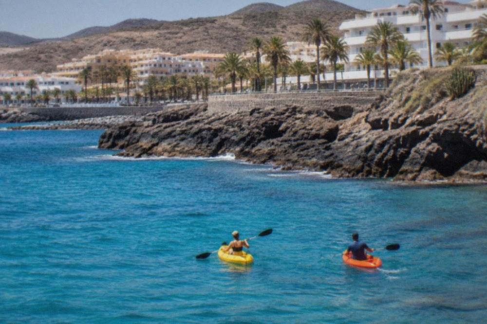 Two kayaks floating on clear turquoise water close to a rocky Tenerife coastline
