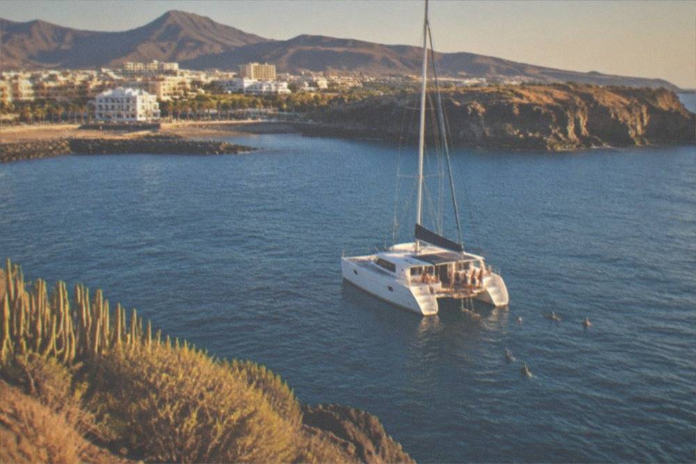 A catamaran flying a flag anchored near cliffs while people snorkel from the stern