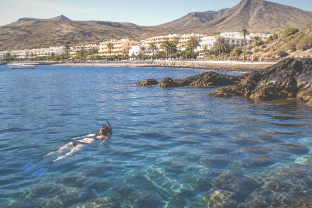 A snorkeller floating face down above a rocky reef with sunbeams in the water