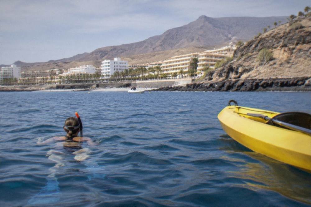 A snorkeller treading water beside a kayak with a coastline of cliffs behind