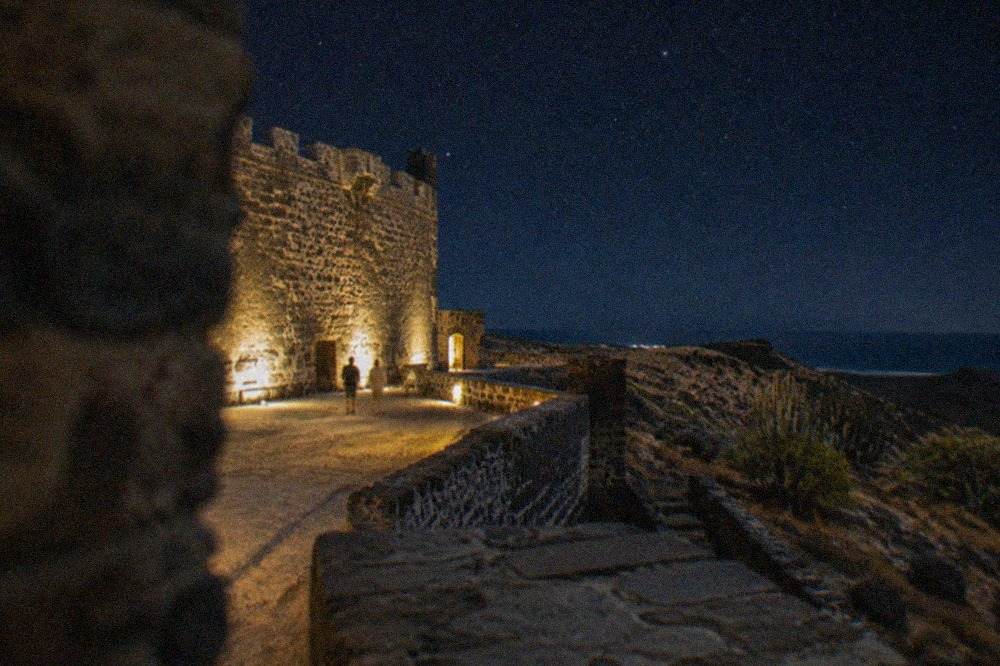 A floodlit castle courtyard at dusk with stone walls and banners