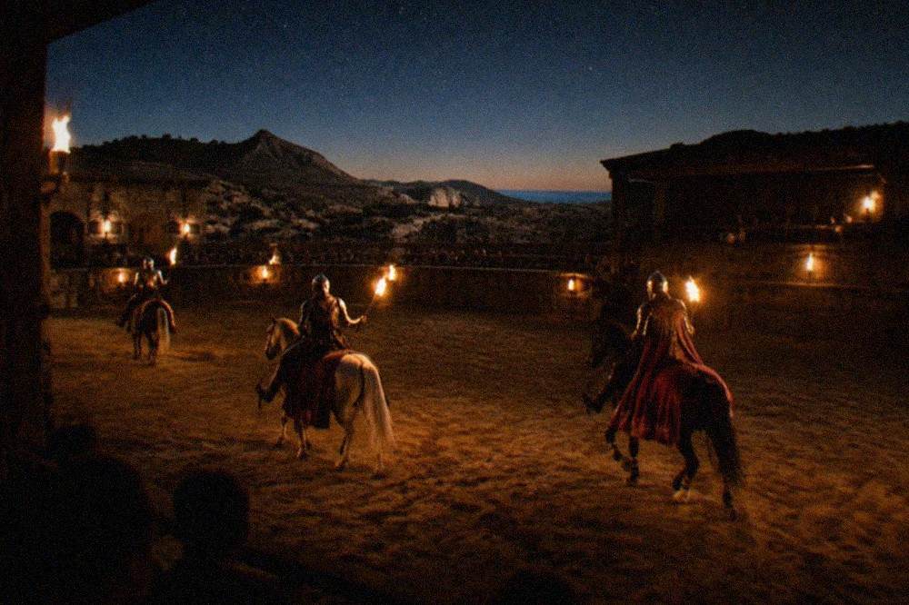 Armoured knights on horseback performing in a torchlit indoor arena