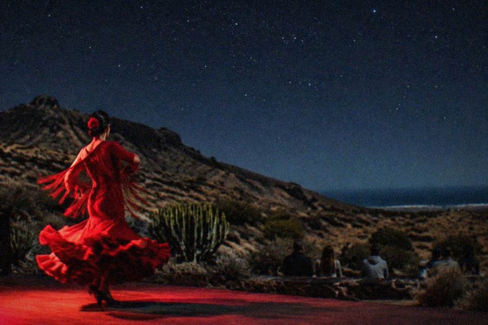 A flamenco dancer mid-turn on a small theatre stage under red lighting