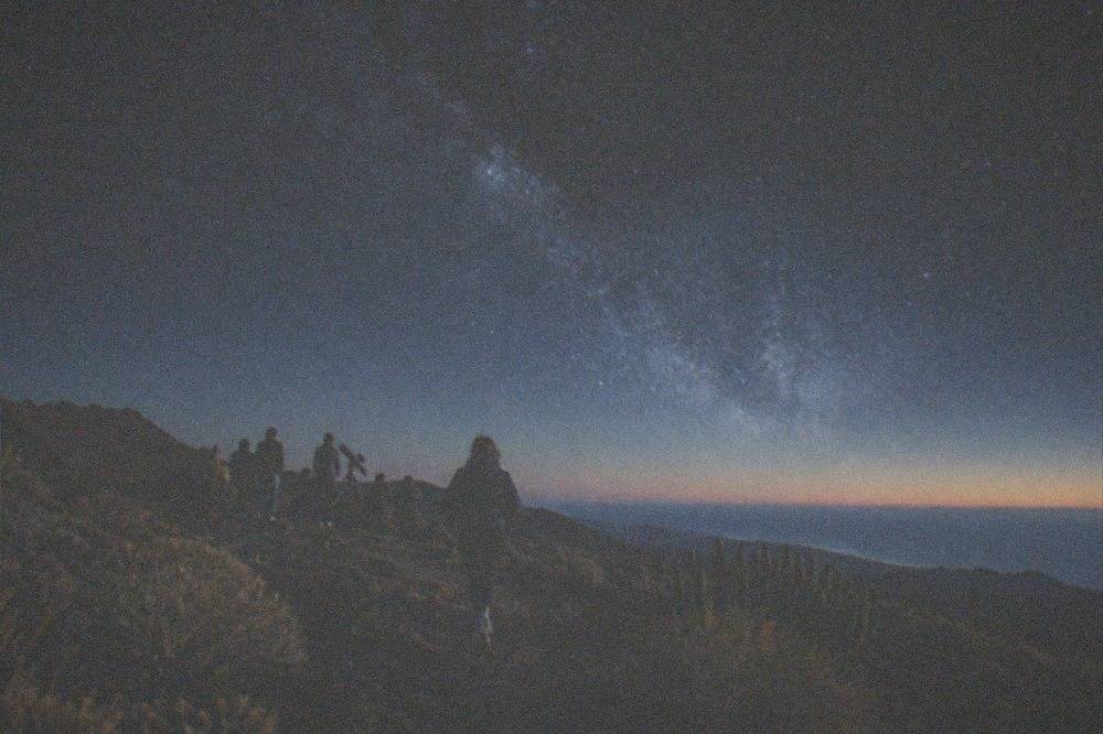 A group of people around a telescope under a star-filled sky on a volcanic ridge