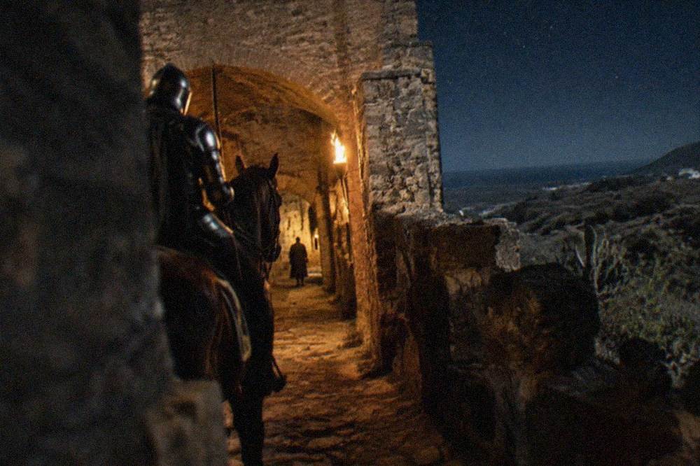 A horse and armoured rider waiting in a torchlit castle corridor