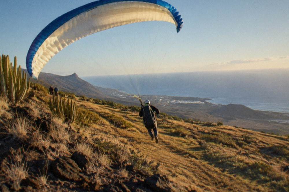 A paraglider canopy inflated on a grassy slope with the ocean far below