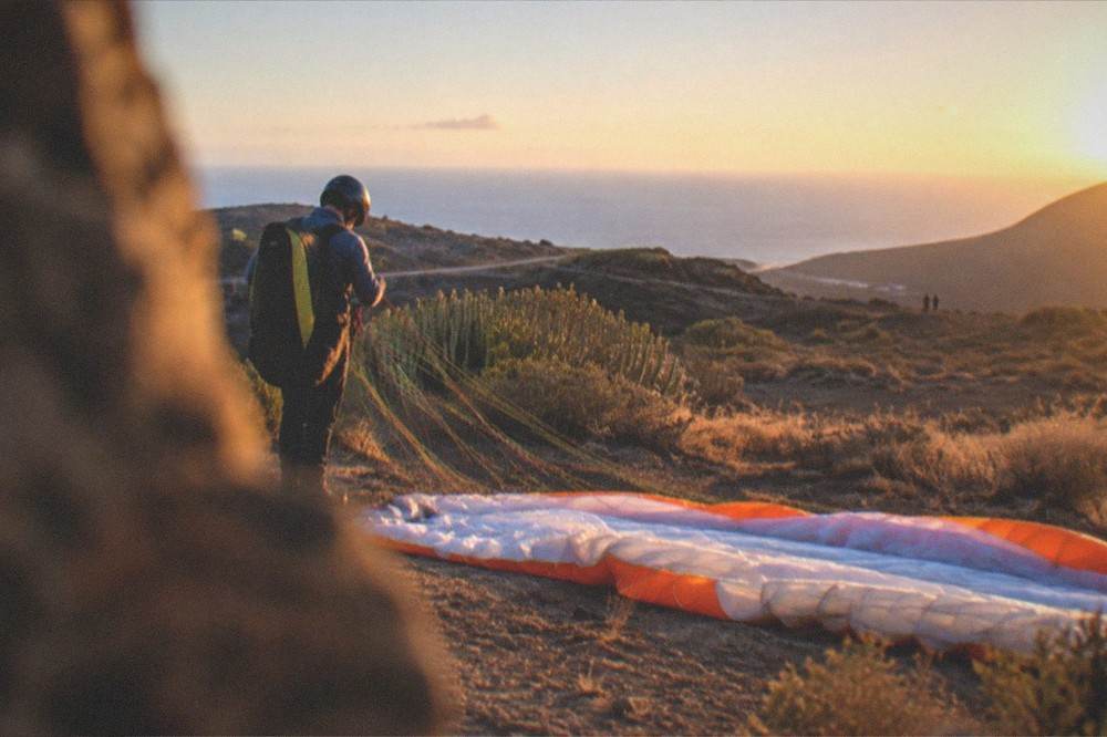 A pilot checking the lines of a laid-out paraglider wing on a launch field before flight
