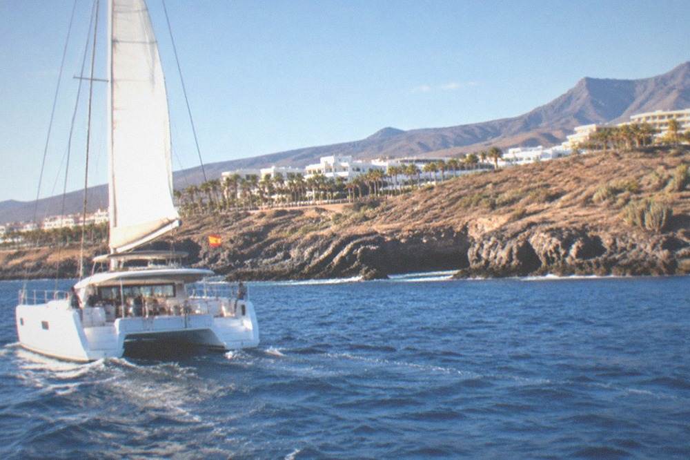 A catamaran flying a small flag cruising along a rocky coastline