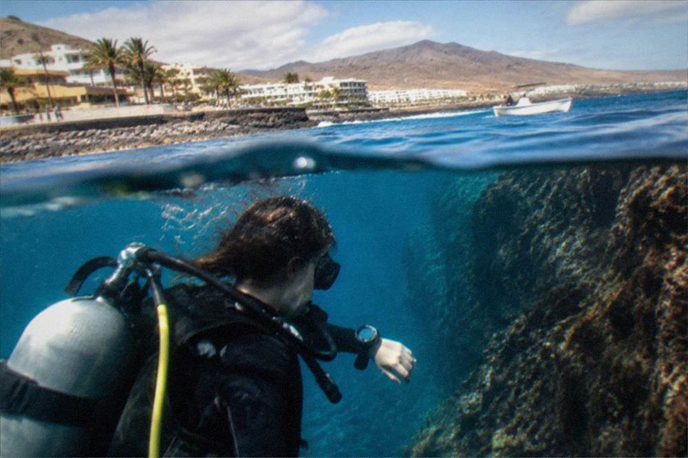 A diver checking a dive computer on a wrist underwater near a rock wall