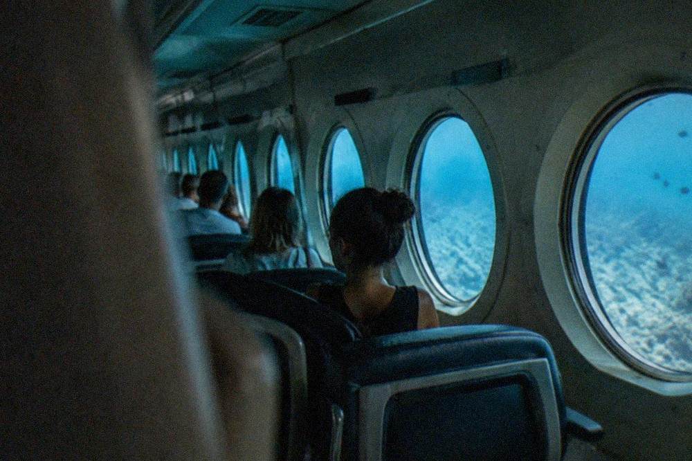 Rows of passengers seated beside round porthole windows inside a submarine cabin