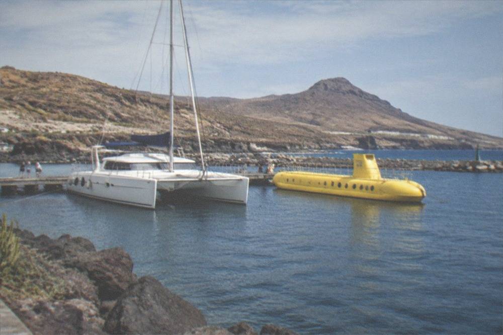 A catamaran and a yellow submarine moored near each other in a small harbour
