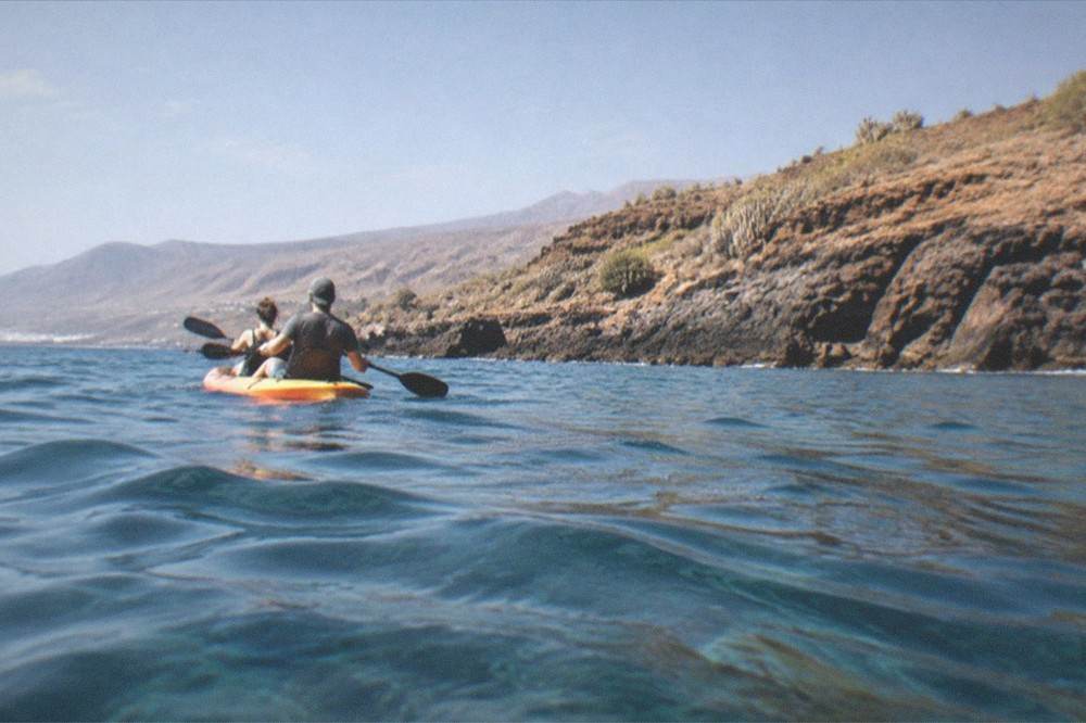 Two people on a kayak near rocky coastline with clear water below
