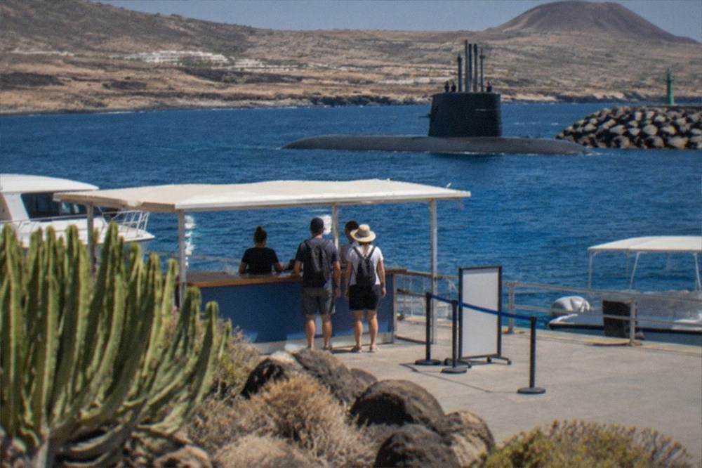 A booking desk at a harbour with a submarine visible on the water behind it