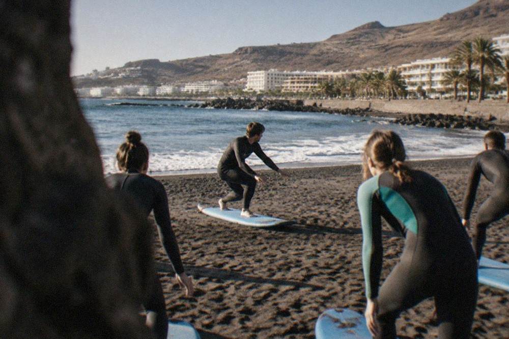 Instructor demonstrating a pop-up stance on a surfboard on the sand with a small group of learners