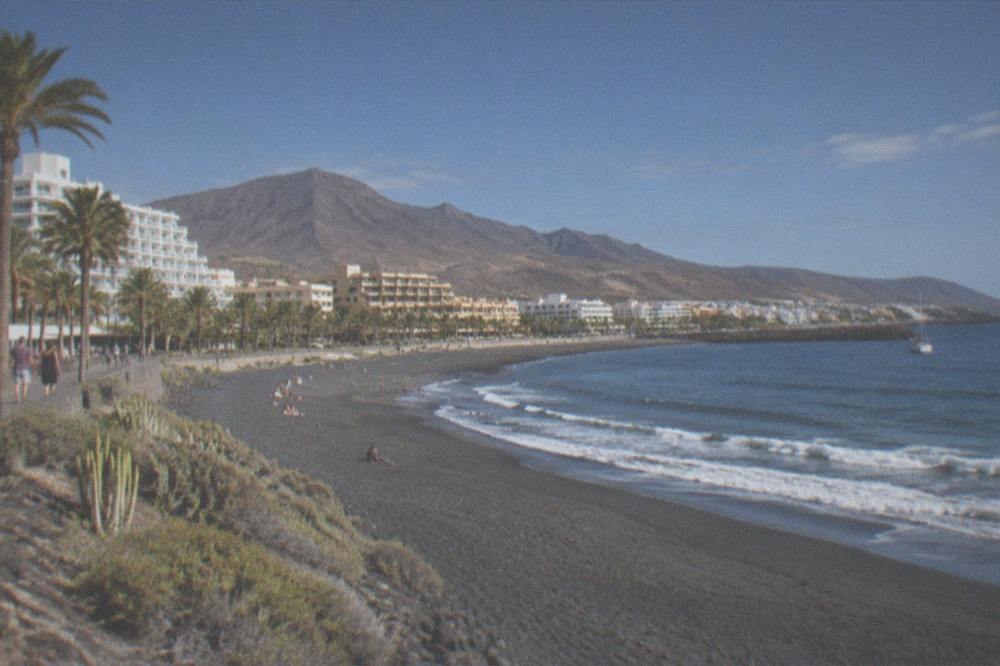Wide view of a southern Tenerife beach town with hotels behind the sand and small waves breaking