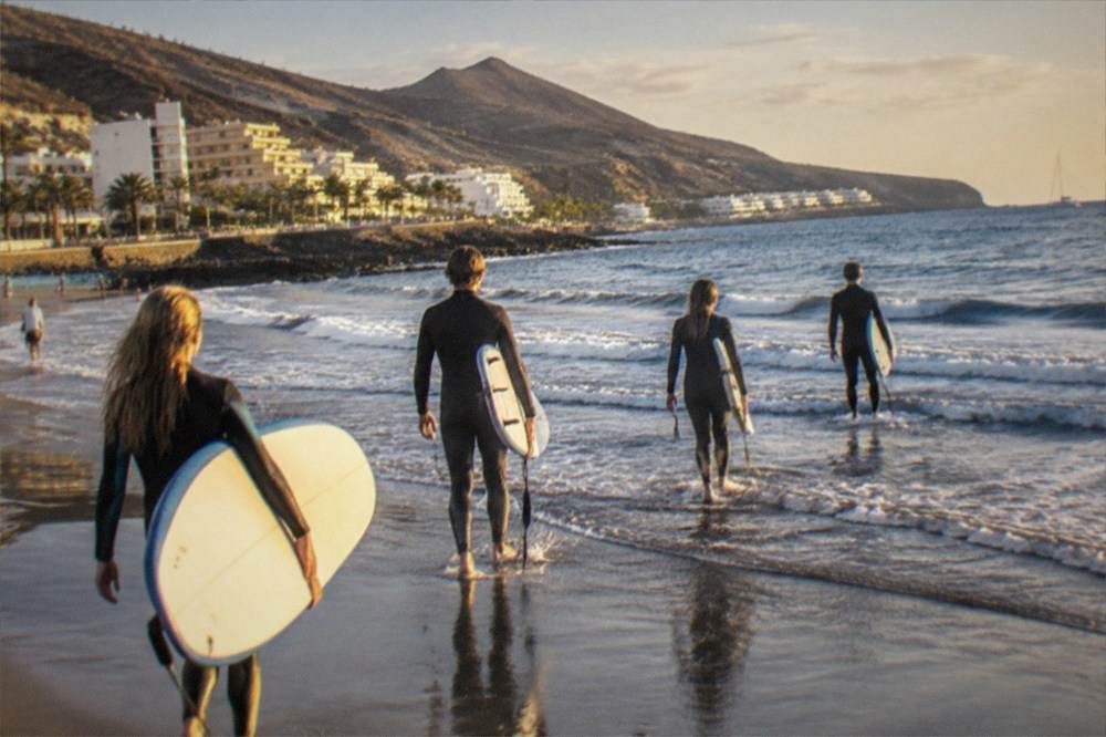 Group of learners carrying surfboards along the water's edge at golden hour