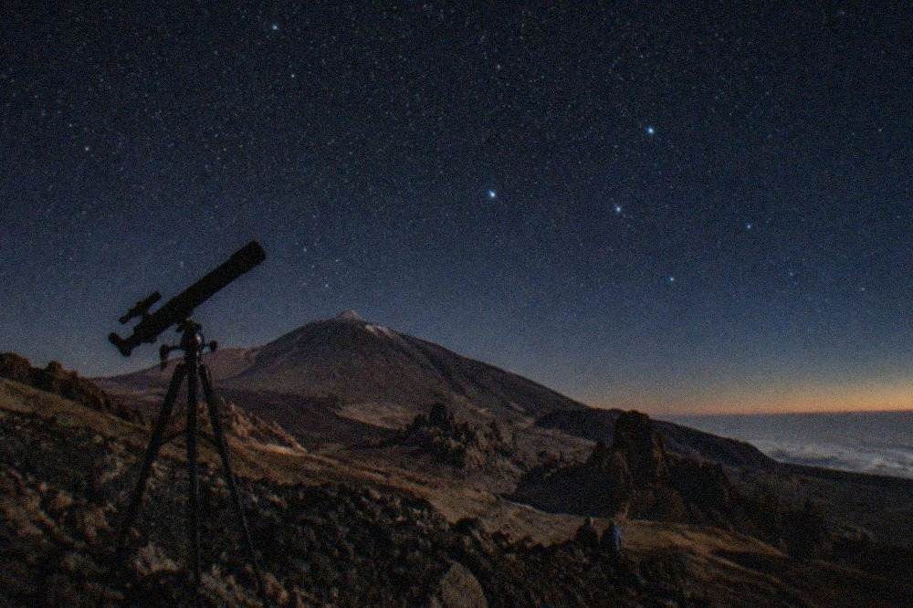 A telescope silhouetted against a star-filled sky above the volcanic slopes of Mount Teide