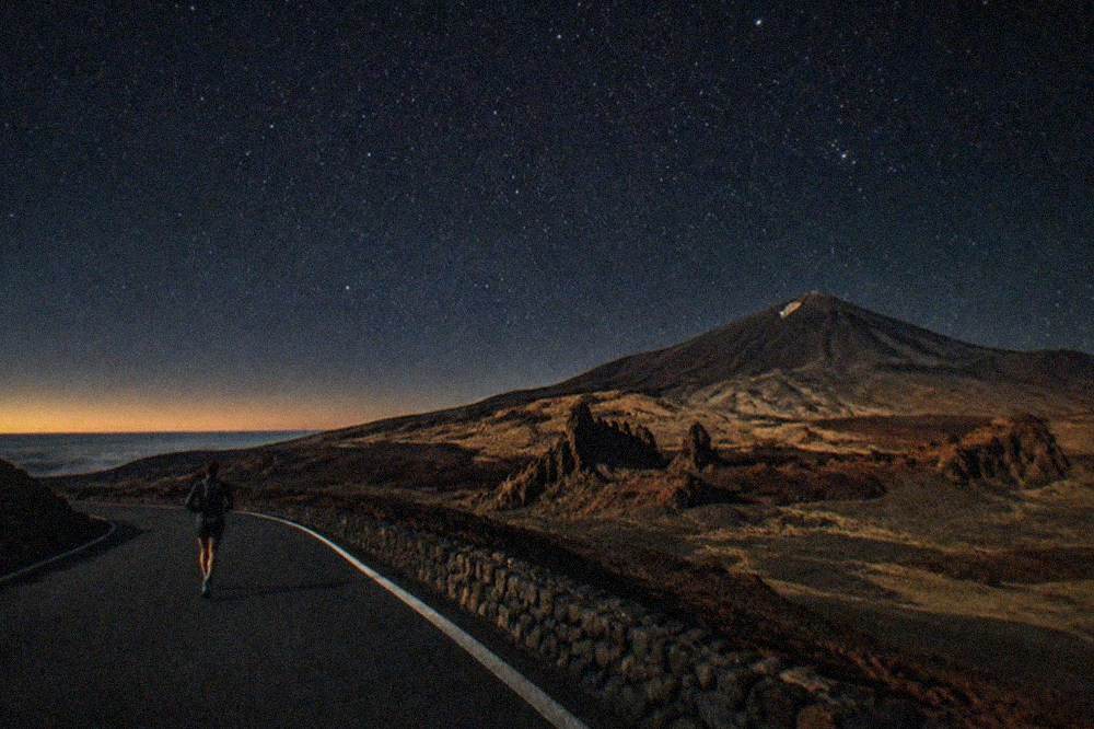 A dark mountain road and empty viewpoint under a dense field of stars on the Teide ridge