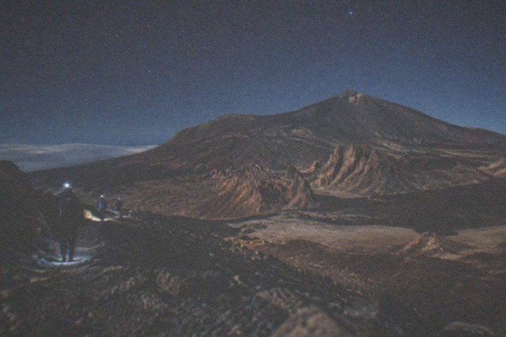Night walkers with head torches on a dark volcanic trail under the stars