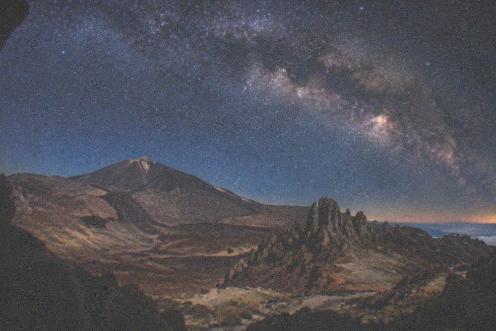 The bright band of the Milky Way stretching across the night sky above dark volcanic rock